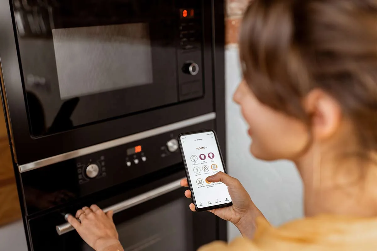 Lady in a kitchen controlling a smart internet connected oven with her phone